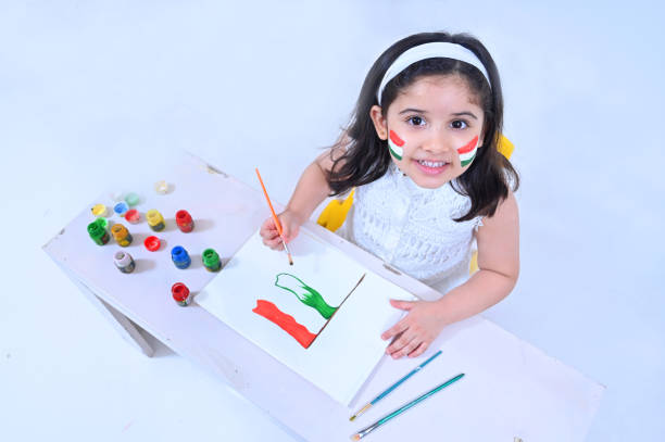 Little girl drawing  Indian flag with poster colors  and looking towards the camera on the occasion of Independence day India